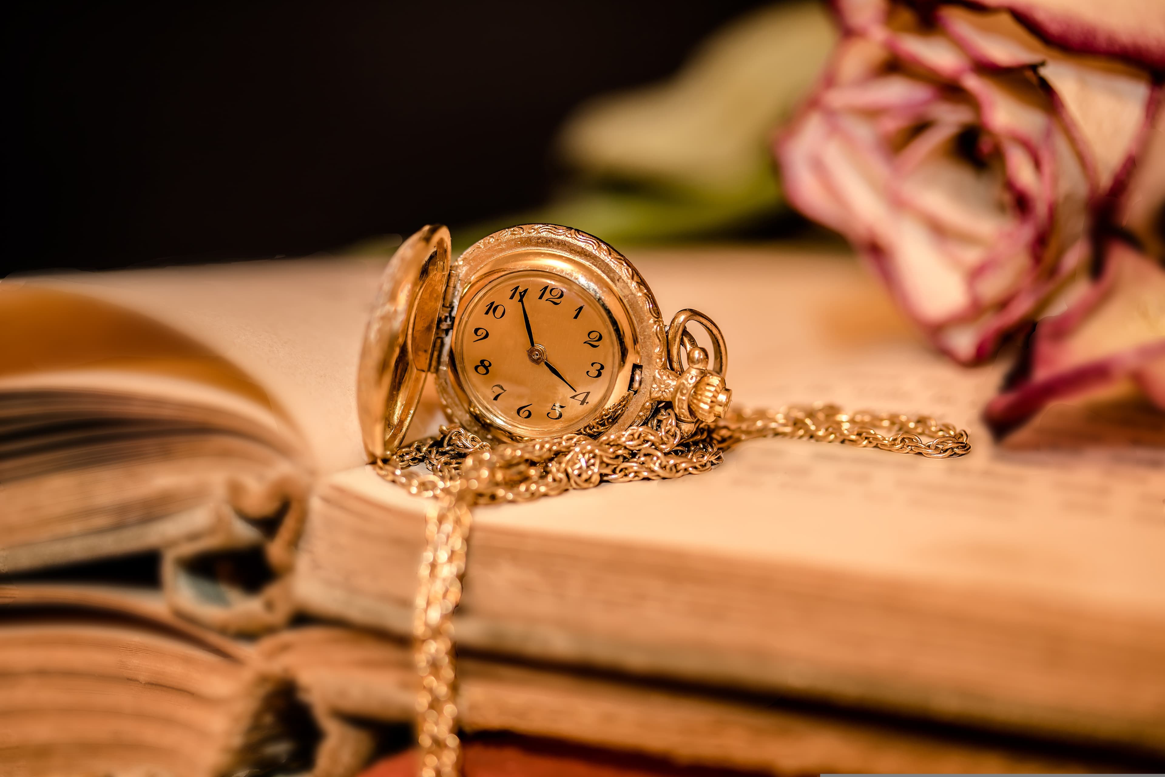An open pocket watch and chain resting on an old book.