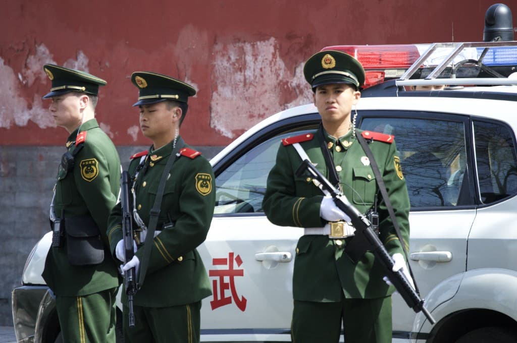 People's Armed Police officers standing beside a patrol vehicle.