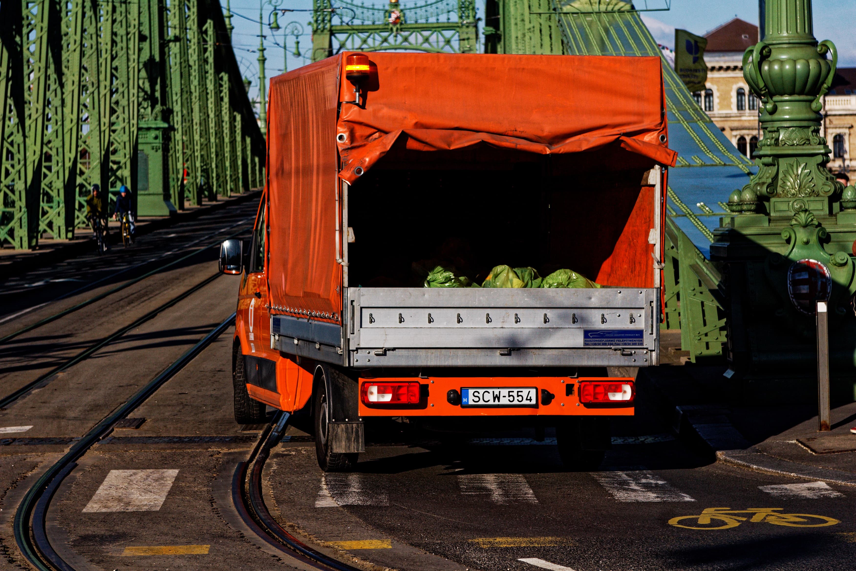 An open flatbed truck carrying sacks of produce across a green iron bridge.