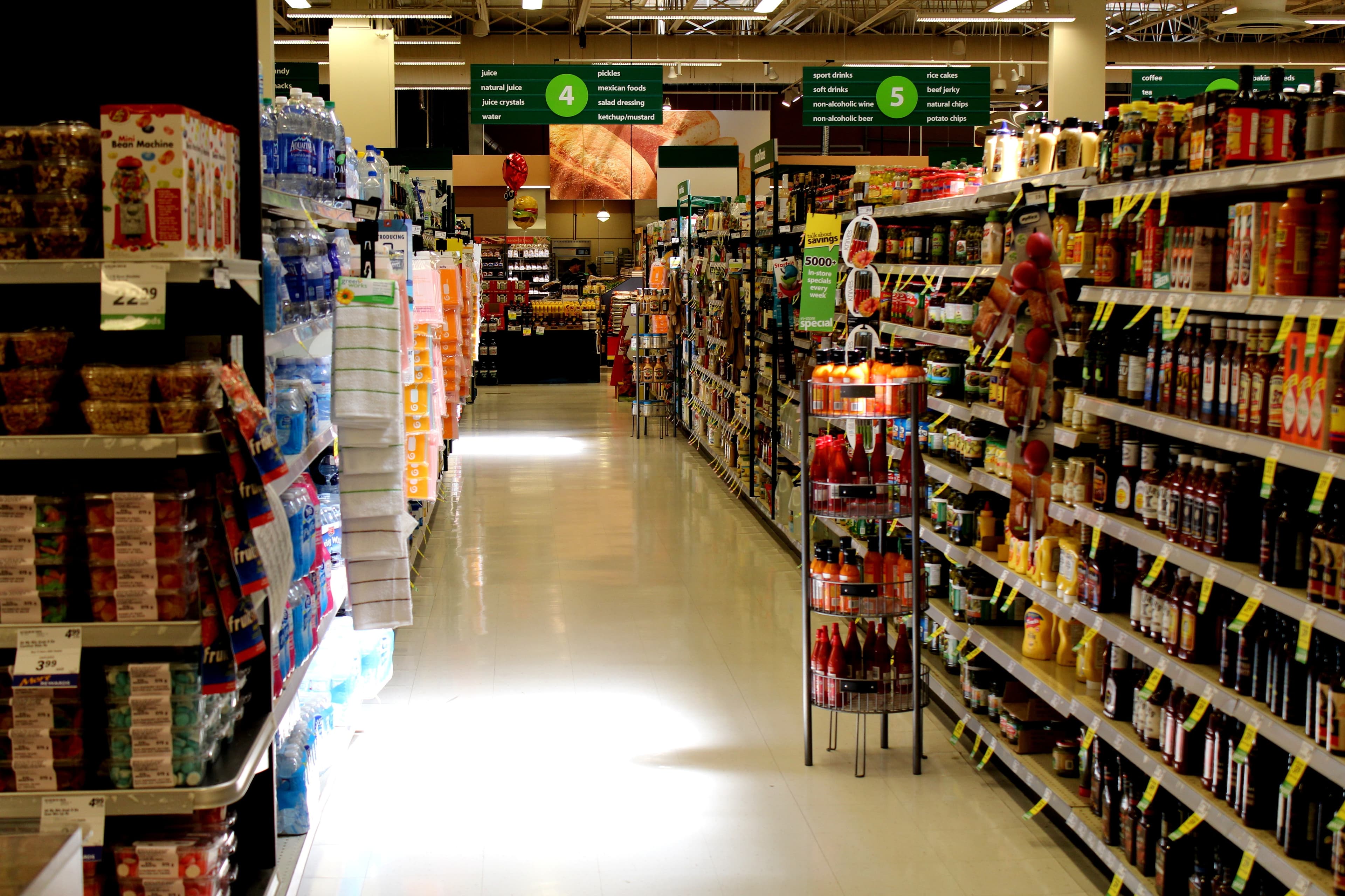 An empty supermarket aisle, shelves of packaged goods running back toward the lit end of the store.